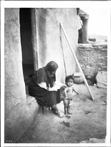 Hopi Indian mother supporting standing baby outside their adobe dwelling, ca.1900