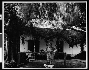 Woman and her dog standing in front of the restored Don Jose Serrano adobe two miles north of El Toro, ca.1930