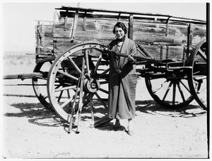 Old woman holding a shotgun in front of a wagon