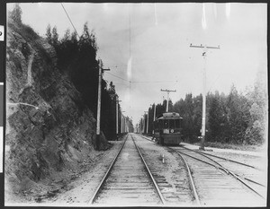 Solitary railway car moving along tracks next to hill, ca.1905