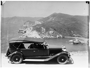 Early-model automobile on a hill overlooking a cove