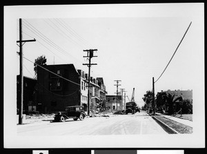 Earthquake-damaged buildings in Compton including the Symphony Theatre, showing trucks and machinery on a street, 1933