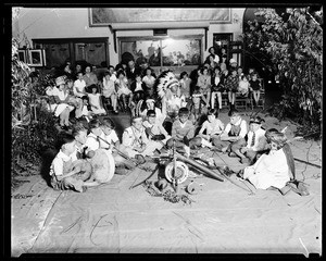 Children gathered around Indian objects and three Indians