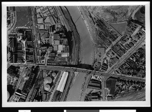 Aerial view of a swollen river passing under a bridge in Los Angeles County, 1938