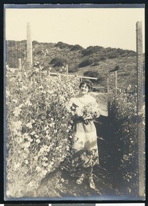 Portrait of a woman in a checked dress near a wall of flowers