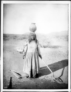 Pima Indian woman, To-Mas-sa, the wife of Ho-Dutch, carrying a pottery jar on her head enroute to planting corn, ca.1900