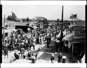 View of Bellflower Boulevard showing commercial shops and a crowd of pedestrians, ca.1912