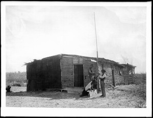 Two men raising (or lowering) a flag in front of the Mexican Custom House, just below the first heading of the Colorado River, near Mexicali, ca.1910