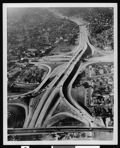 Low-altitude aerial view of the 4-level interchange where the Hollywood Freeway (U.S. 101) and the Pasadena/Harbor Freeway (SR 110) meet; Los Angeles, ca.1950-1959