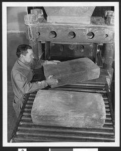 Shell Oil Company employee at work, showing a man moving slabs of rock across a machine, ca.1940