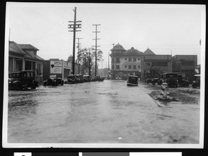 Flooded street, showing automobiles parked along the sides of the road