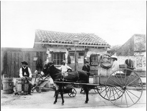 The "Vegetable Woman" and her donkey cart in front of an adobe building, ca.1885