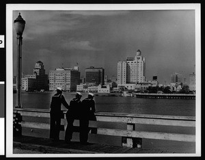 Three sailors looking at the Long Beach skyline from a pier, ca.1940