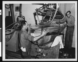 Interior of an unidentified factory, showing two factory workers gripping a large piece of equipment, ca.1935