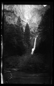 Small waterfall near large clusters of trees, showing river in foreground, Yosemite National Park, California