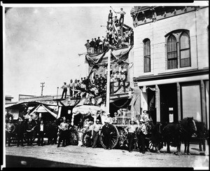 Portrait of fire fighters and their engine posed on and in front of a brick building on the southeast corner of First Street and Main Street, ca.1885