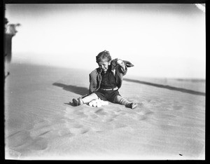 A young boy sitting on a sandy ground with a pile of what appear to be eggs