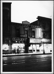 Exterior view of the lit Pico Building on Main Street at dusk or dawn, showing streetcar tracks, ca.1938