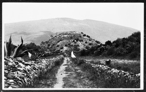 Unidentified path leading to a hill and large mountain, showing a silhouette in the background