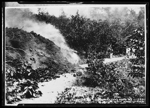 Lava creeping over a curved road after the eruption of Maui Loa, showing a small group of people standing nearby, Hawaii, April 1926