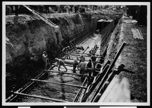 Workers manipulating concrete in the bottom of a trench during storm drain construction