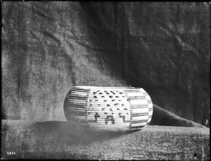 Indian basket displayed in front of a cloth backdrop, ca.1900