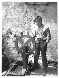 Nino Majel standing beside a carillon wheel at Mission San Juan Capistrano, California, ca.1905