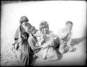 Apache Indian grandmother carrying her grandchild on her back and three others sitting nearby, Palomas Indian Reservation, 1903