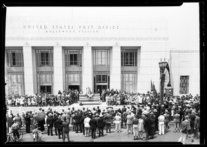 Man giving a speech to a crowd on the steps of the United States Post Office in Hollywood