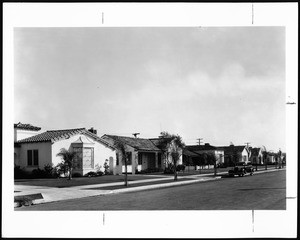 View of a street of single-story residences in Los Angeles, showing paved street and automobile, ca.1935