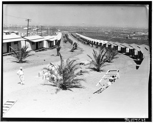 Men painting a row of small wooden buildings along a dirt road