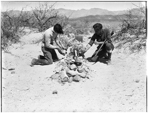 Two men bent over a grave in the desert