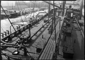 Oil being exchanged between a ship and a wharf at the Standard Oil Company docks, ca.1920