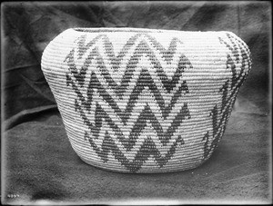 Indian basket displayed in front of a cloth backdrop, ca.1900