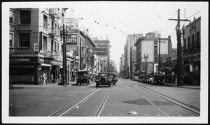 View of commercial Sixth Street near Grand Avenue, looking east, showing automobiles and streetcar tracks, ca.1920