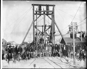 A group of miners (forming a mine shift) pose in front of mine headframe (shaft), Goldfield, Nevada, ca.1905