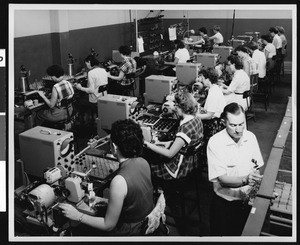 Lines of women workers at the Acme Electronics company, showing a man standing in the foreground, ca.1940