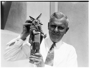 Grinning man holding a Native American kachina doll at the Pacific Southwest Museum