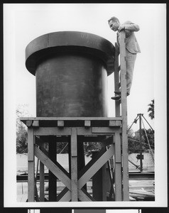 Exterior view of a man looking into a large rimmed pipe, ca.1940