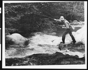 Trout fisherman fishing from a rock in a stream, ca.1930