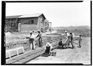Men renovating the San Fernando Mission, showing adobe brick makers at work in the foreground, 1927