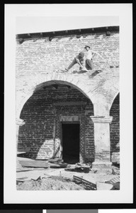 Two men working on a stone arch of the Mission San Juan Capistrano during reconstruction under Reverend John O'Sullivan