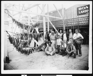 Men holding fishing gear pose next to their catch, ca.1930