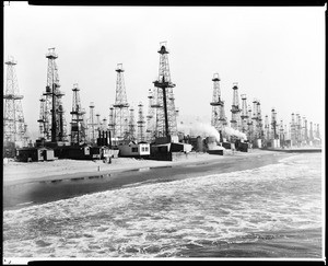 View of oil derricks along the coast of Playa del Rey in Venice, showing storage tanks and many low buildings, ca.1925