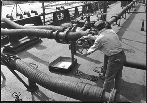 Flexible pipes manipulated by a man on the deck of what may be a boat