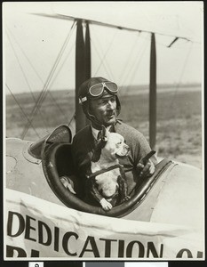 Pilot posing with a dog in a cockpit, ca.1925