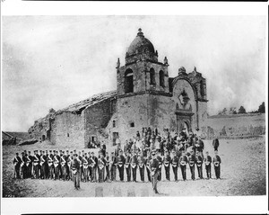 Portrait of soldiers, bandsmen and civilians posing in front of the Mission San Carlos for the exhuming of Friar Junipero Serra's remains, Monterey, July 3, 1882