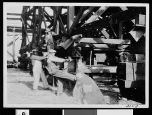 Workers using a screw mechanism to raise a wooden structure, ca.1930