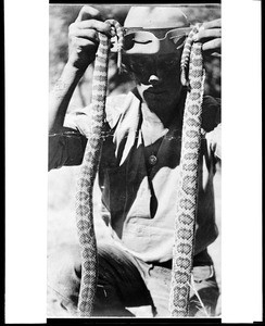 Portrait of Bosco, teamster for the survey of the Los Angeles Aqueduct Railroad, holding two rattlesnakes, 1907