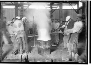 Factory workers gathered around a steaming pot of molten metal